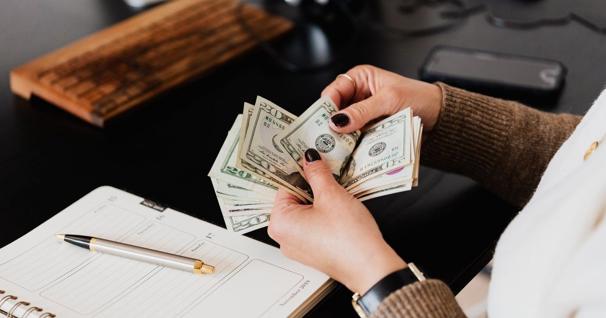 A person counts US dollar bills over an open notebook at a desk, the kind of hourly pay math behind caregiver wage decisions.