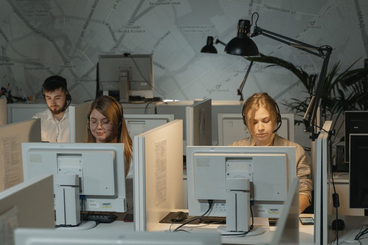 Three answering service receptionists wearing headsets work at computer stations in a shared call center office.